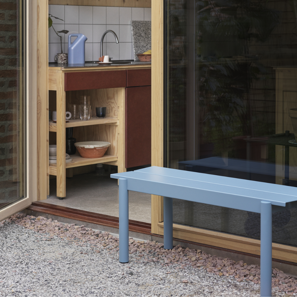 The pale blue Linear Steel Bench from Muuto outdoors beside an entryway.