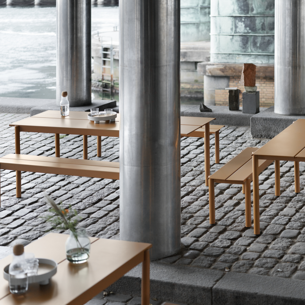 The burnt orange Linear Steel Table from Muuto in an outdoor business space.