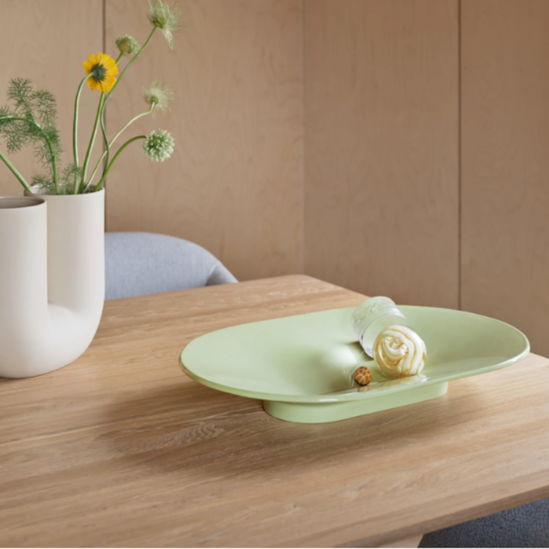 The wide Mere Bowl from Muuto in light green on a dining table.