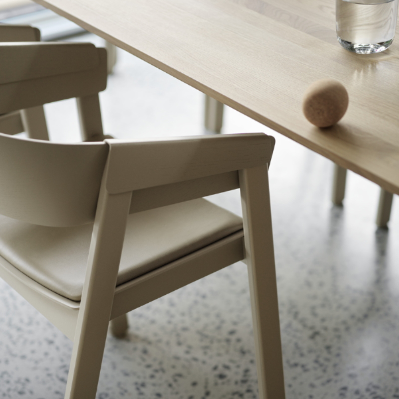 The Upholstered Cover Armchair from Muuto in dark beige with stone refine leather at a dining table.