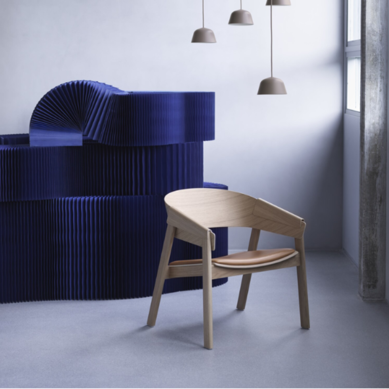 The Upholstered Cover Lounge Chair from Muuto with cognac refine leather in oak in a living space.