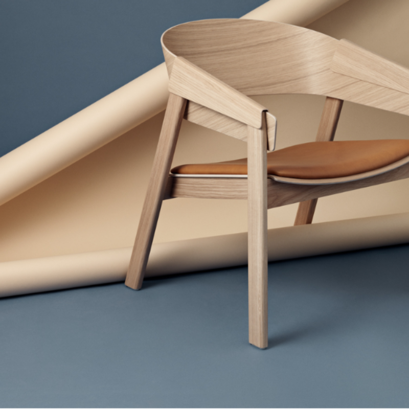 The Upholstered Cover Lounge Chair from Muuto with cognac refine leather in oak in a studio.