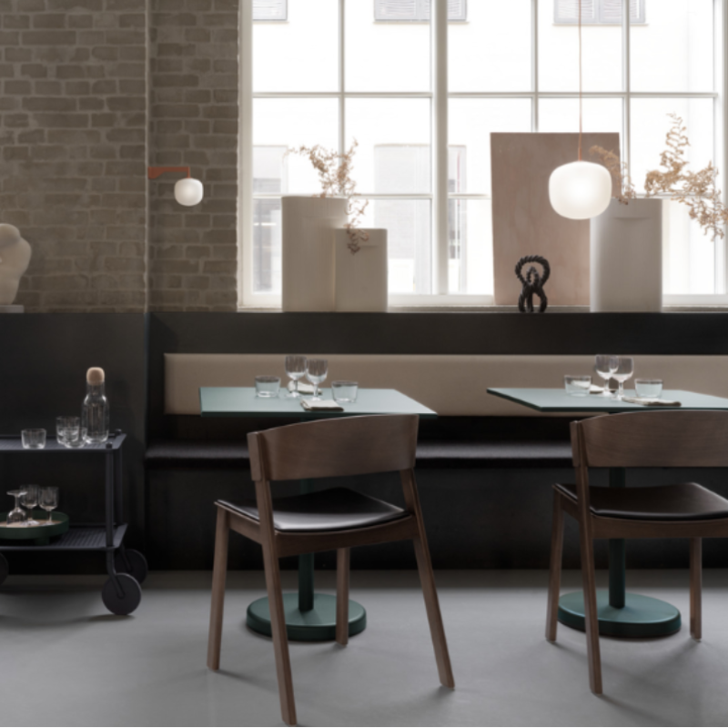 The Upholstered Cover Side Chair by Muuto with black refine leather in dark stained brown in a restaurant.