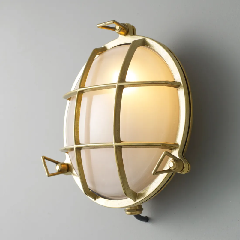 The medium Brass Bulkhead Outdoor Wall Sconce from Original BTC in polished brass in a studio from an angle turned on.