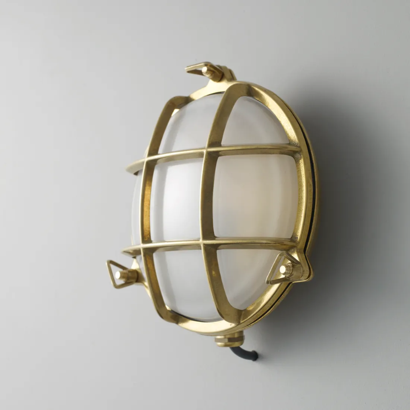 The small Brass Bulkhead Outdoor Wall Sconce from Original BTC in polished brass in a studio from an angle.