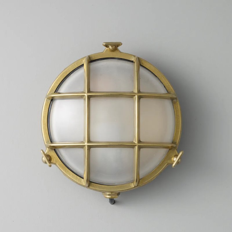 The small Brass Bulkhead Outdoor Wall Sconce from Original BTC in polished brass in a studio.