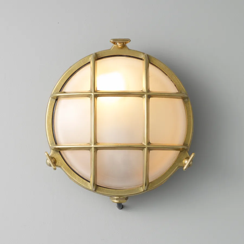 The small Brass Bulkhead Outdoor Wall Sconce from Original BTC in polished brass in a studio turned on.
