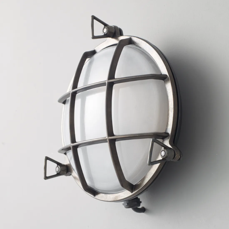 The medium Brass Bulkhead Outdoor Wall Sconce from Original BTC in weathered brass in a studio from an angle.