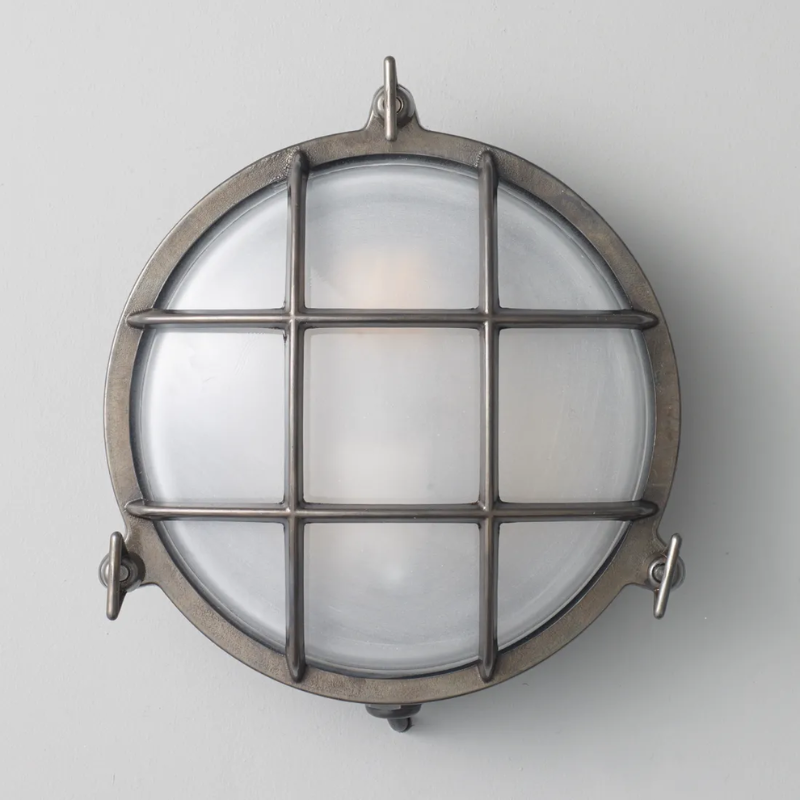 The medium Brass Bulkhead Outdoor Wall Sconce from Original BTC in weathered brass in a studio.