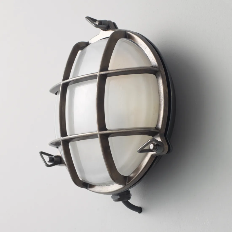 The small Brass Bulkhead Outdoor Wall Sconce from Original BTC in weathered brass in a studio from an angle.