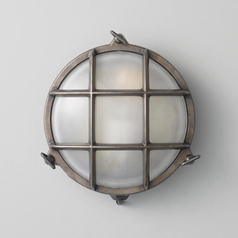 The small Brass Bulkhead Outdoor Wall Sconce from Original BTC in weathered brass in a studio.
