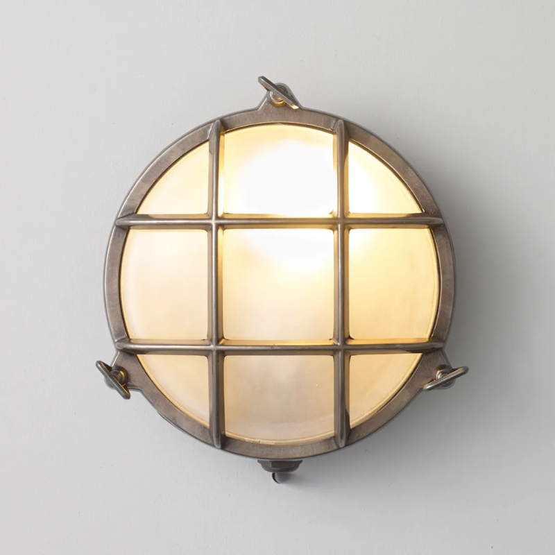 The small Brass Bulkhead Outdoor Wall Sconce from Original BTC in weathered brass in a studio turned on.