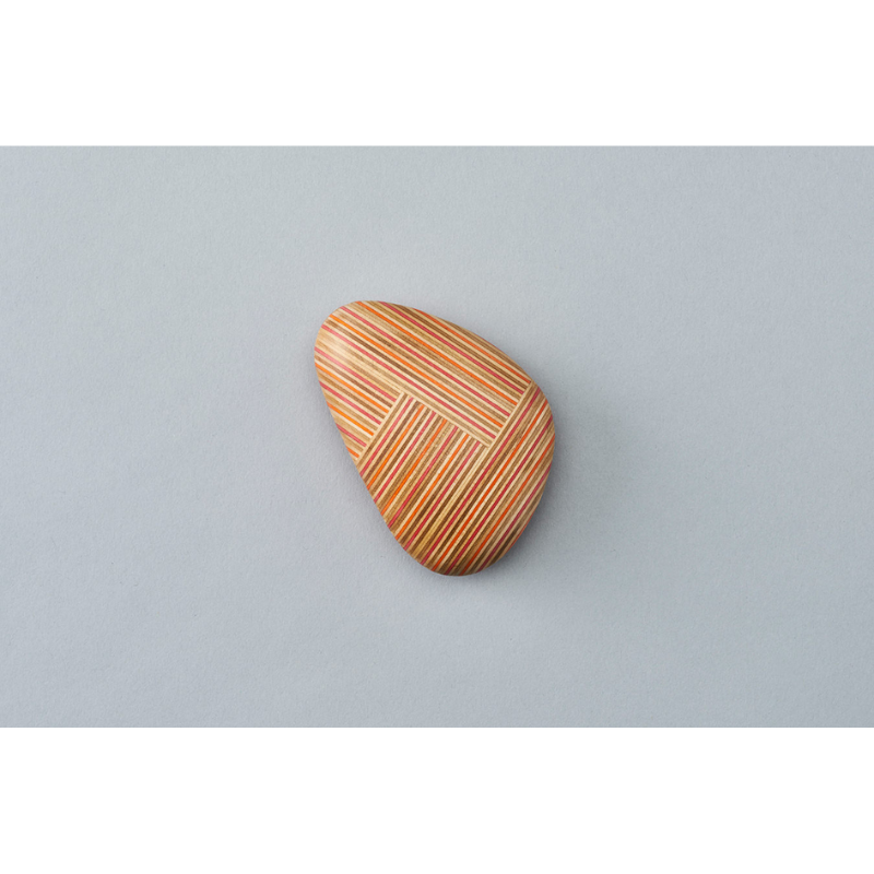 The Koishi Paperweight from Plywood Laboratory triangle shape in red orange within a studio.