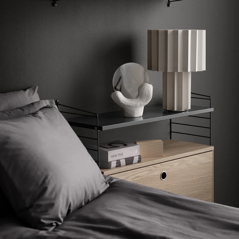 The shelves from String Furniture in dark grey used for a bedside table.