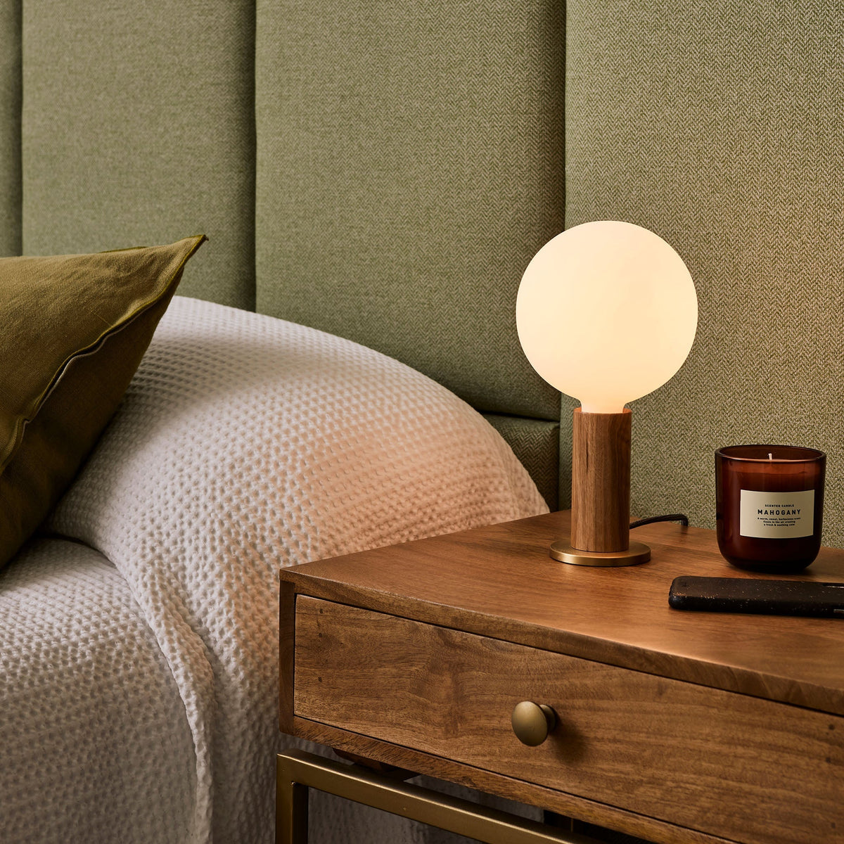 The Sphere IV E26 Dim-to-Warm LED Bulb by Tala Lighting in a walnut table base next to a bed.