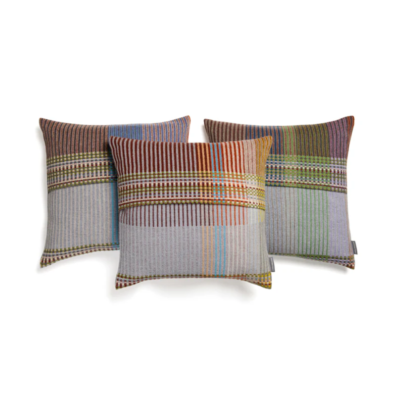 The Joan Cushion features a calm duo of a light grey and burnt sienna, separated by areas of a vibrant mossy green with small highlights of pale yellow and blush sprinkled throughout.