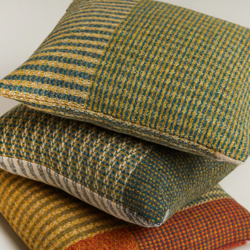 The Lismore Cushion by Wallace & Sewell features a blend of woven green, red, and yellow natural fibers.