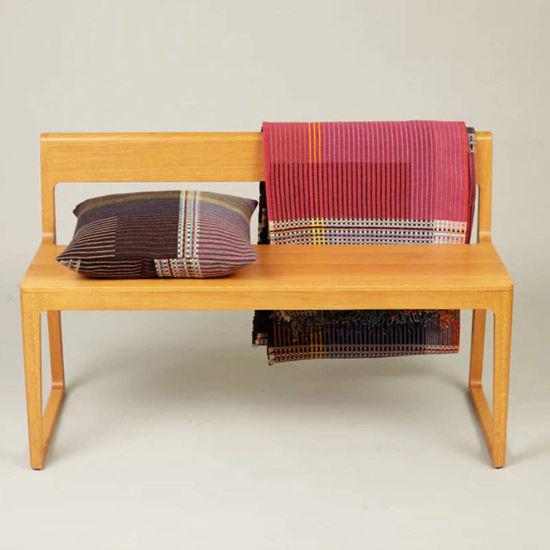 The Sophia Throw by Wallace & Sewell with matching throw pillow on a bench.