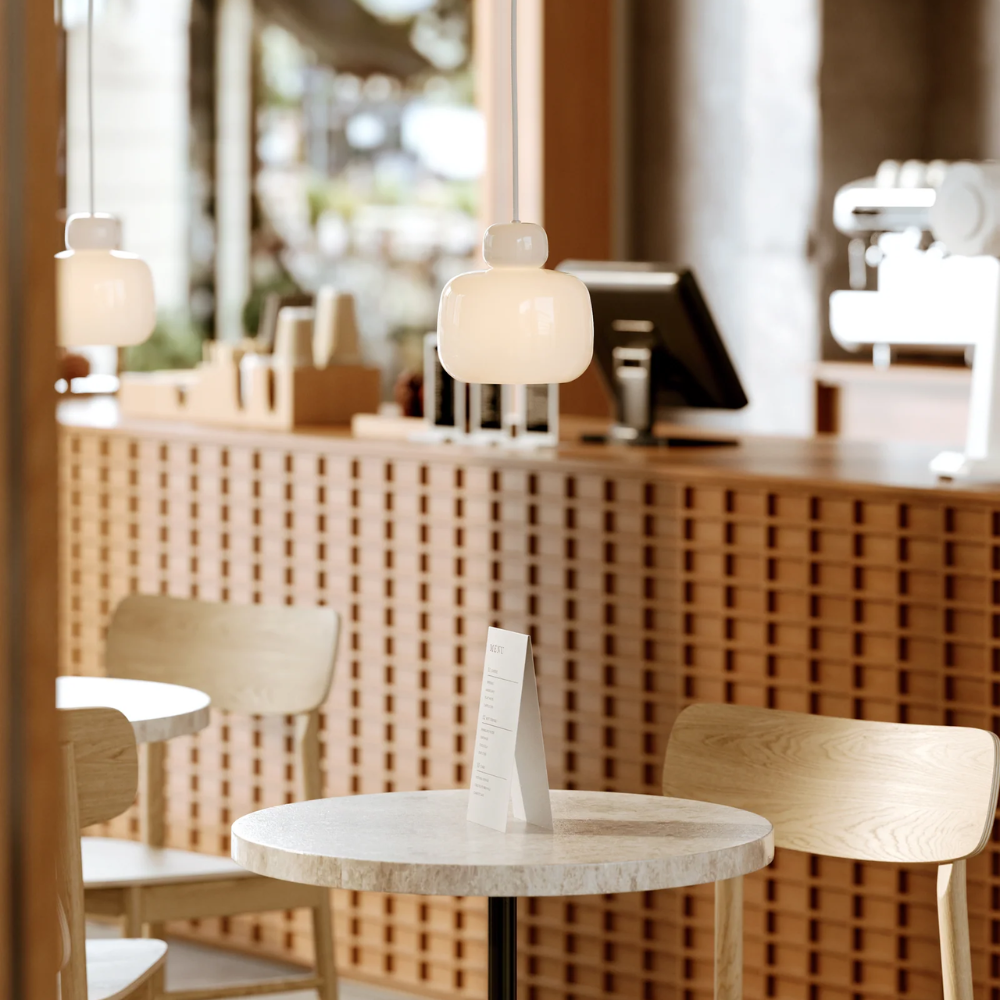 The Stone Glass Pendant in the size Small by Woud over a cafe table in a coffee shop.