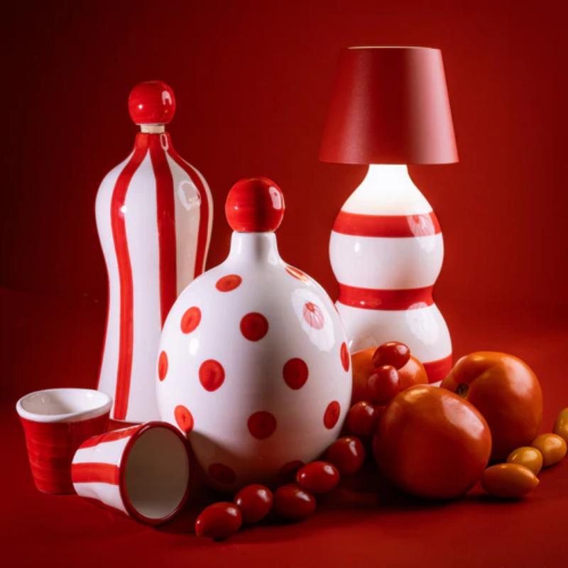 The red Poldina Pro Stopper from Zafferano with decorative bottles in a studio.