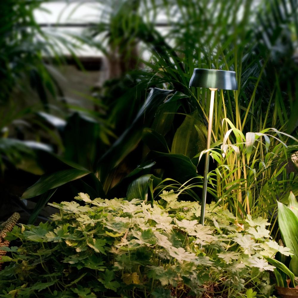 The anodized green Sister Light Wi-Fi Garden Lamp from Zafferano outdoors in a garden.