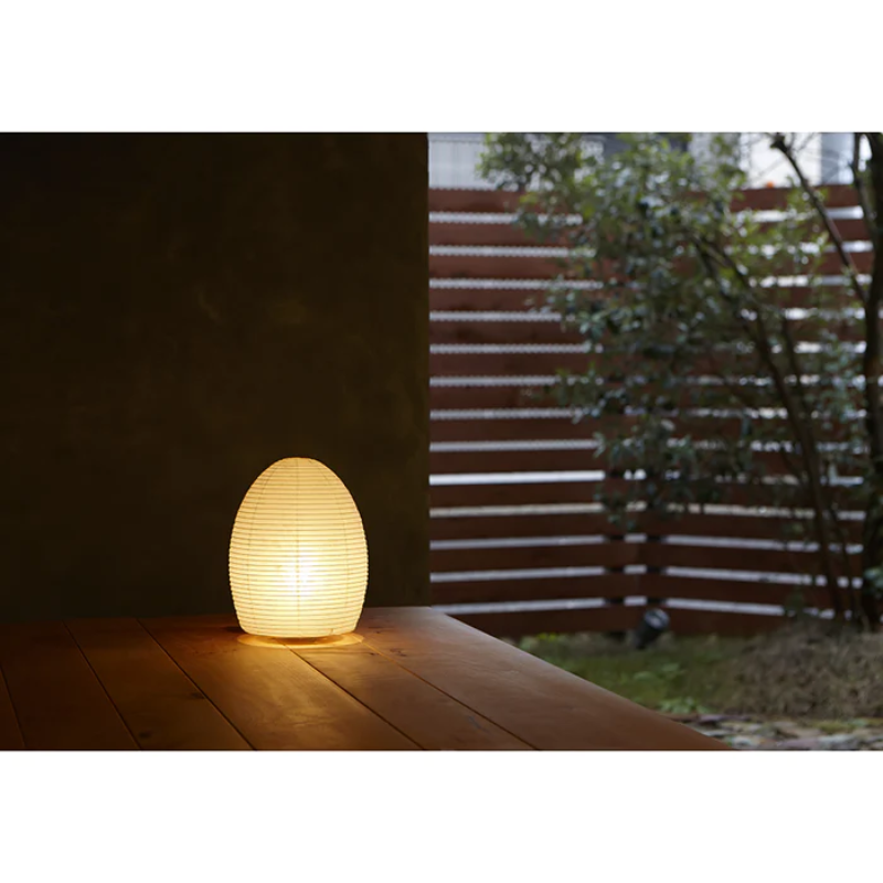 The Paper Moon 1 lamp by Asano outdoors on a porch within a garden at night time, turned on.