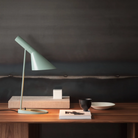 The AJ Mini Table Lamp from Louis Poulsen on a desk lifestyle photograph.