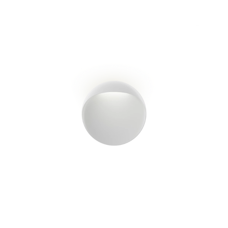 The Flindt Wall is distinguished by a light egress from an opening in the top that emits light down the front of the fixture, creating a subtle, glowing ring of reflected light on the transition between the concave and convex shapes. The oval shape is lifted off the mounting surface, giving the fixture a floating appearance.