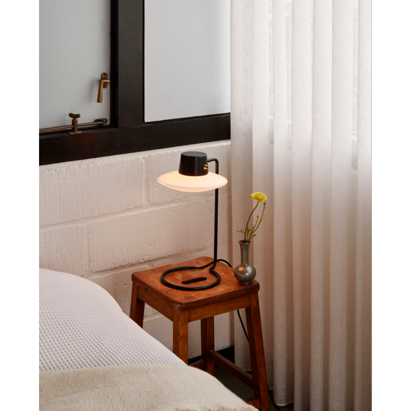 The AJ Oxford Table Lamp emits a pleasant downwardly directed light, which harmoniously illuminates the surface below it through the soft transparency of its triple-layered hand-blown opal glass. In the variant without the top metal shade, the milky opal-glass shade provides further glow to form an alluring halo around the fixture.