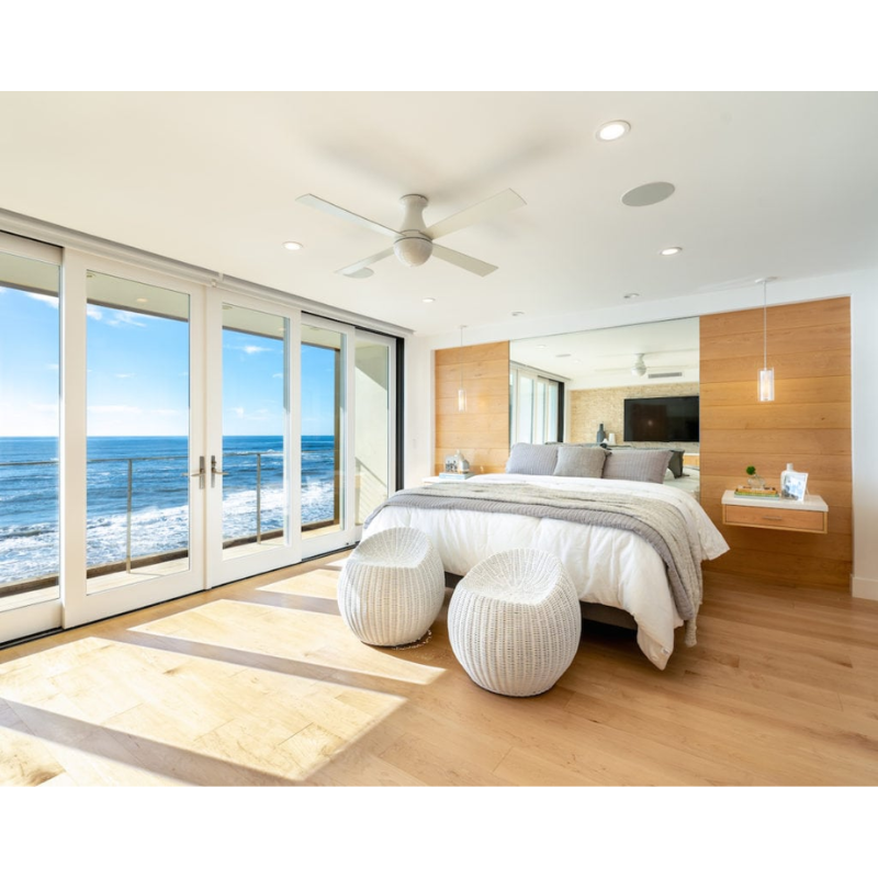 The Ball Flush ceiling fan from The Modern Fan Co. with 42" blades and the LED option. This fan has the gloss white fan finish, and white blade color within a bedroom next to the ocean on the coast.