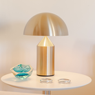 This is the Atollo Gold Table Lamp from Oluce turned on nestled on a small table.