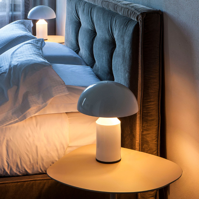 This is the Atollo Metal Table Lamp from Oluce in White turned on at night beside a bed.