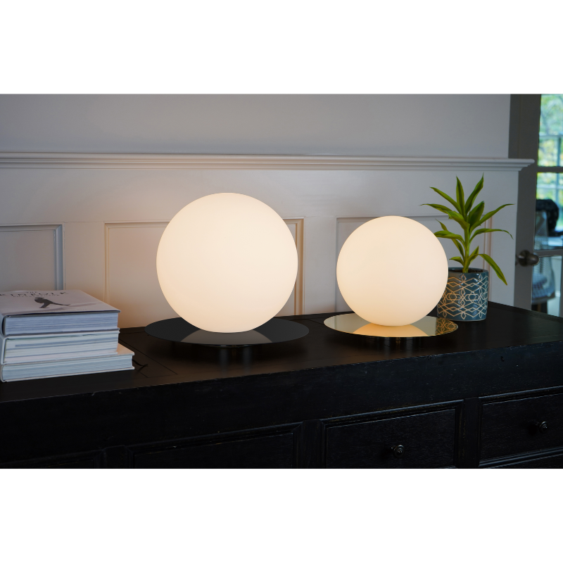 Two different size and color Bola Sphere Table lights from Pablo Designs here are featured on a table within a living space.