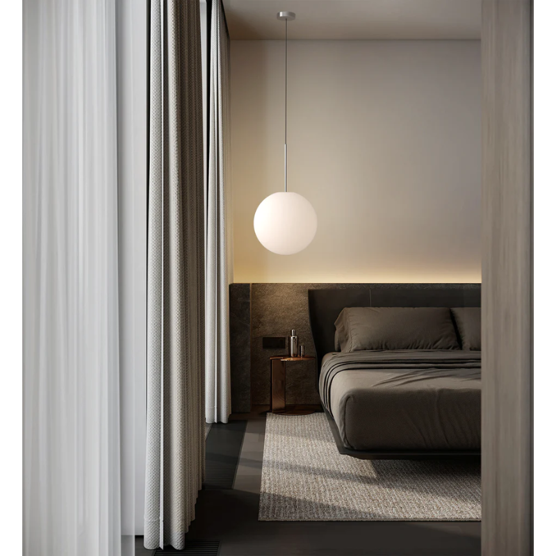 The Bola Sphere from Pablo Designs next to a bed inside of a bedroom.