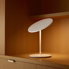 The Circa Table light from Pablo Designs on a bookshelf, gently illuminating it.