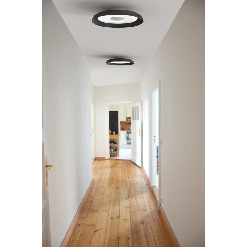 Two black Nivél Flush lights from Pablo Designs mounted to the ceiling in a hallway.