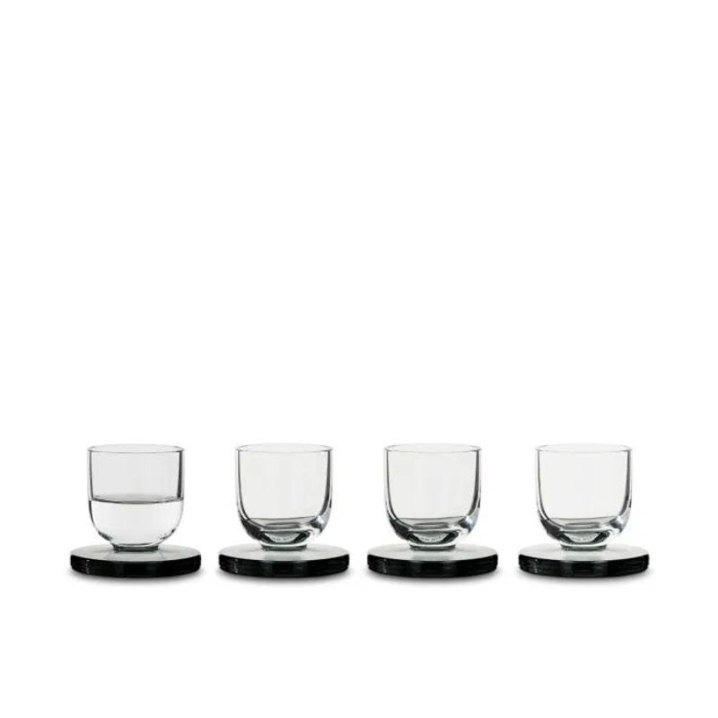 A set of four Puck Shot Glasses from Tom Dixon, with one of the four half filled with the other three empty.