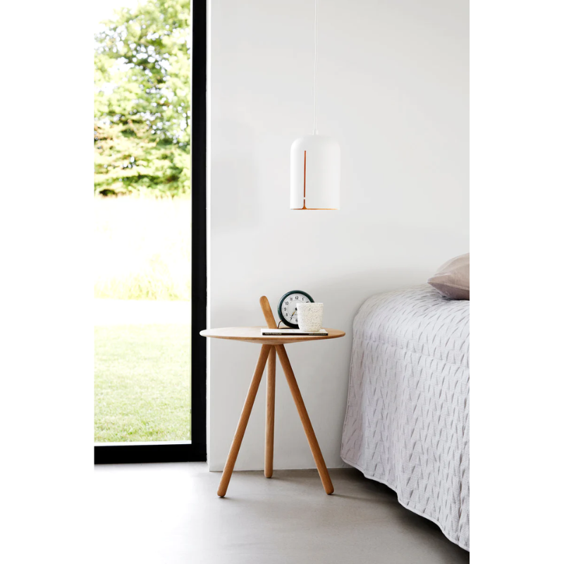 The Come Here Side Table in White Pigmented Oak next to a bed.