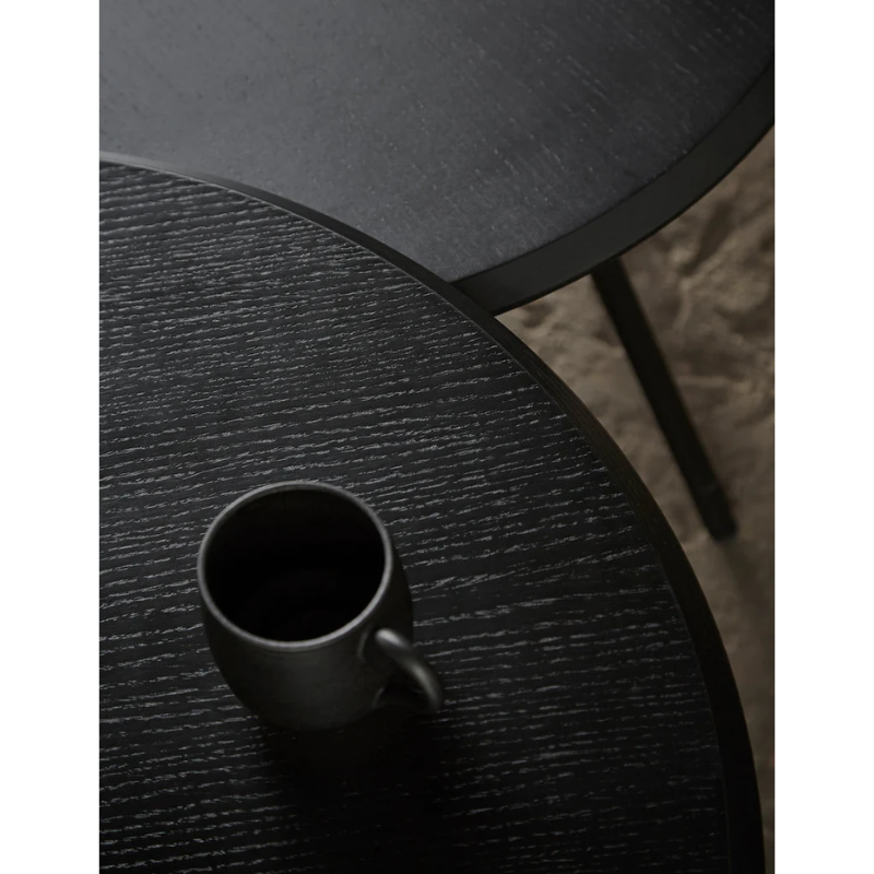 A black Soround Coffee Table from Woud being used for a drink.