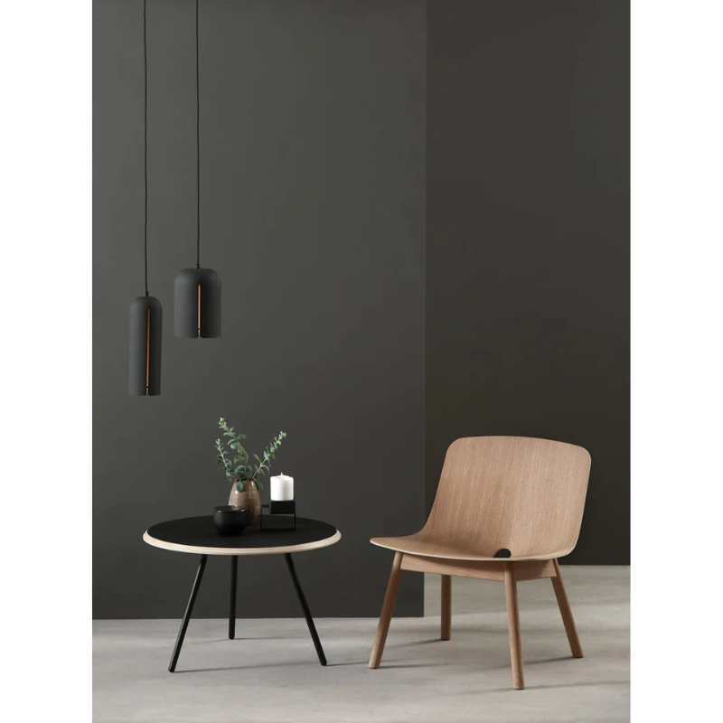 A black Soround Coffee Table from Woud next to a chair.