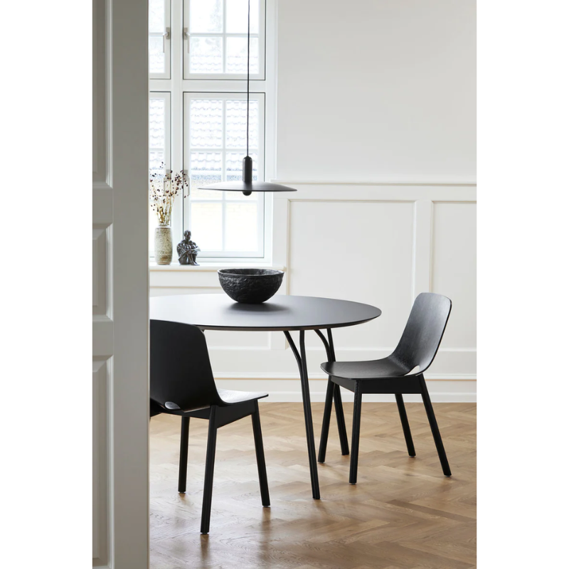 The black Tree Dining Table from Woud underneath a pendant light in a dining space.