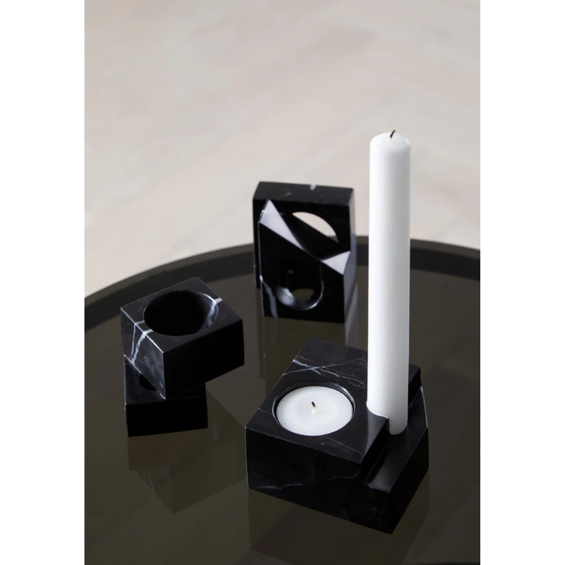 A photograph of the solid marble Jeu De Dés 2 Candle Holder by Woud on top of a glass tabletop, showing off the entire collection of candle holders.