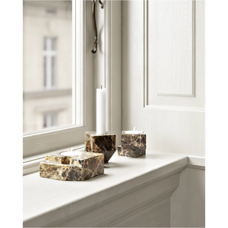 A photograph of the solid marble Jeu De Dés 2 Candle Holder by Woud in brown on a windowsill of a living room.
