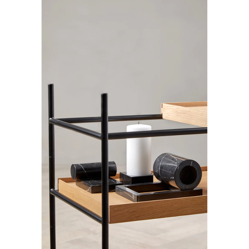 The Jeu De Dés 3 Candle Holder from Woud, made from solid marble with a pillar candle on a bookshelf with the black Booknd.