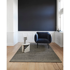 The Rombo Rug from Woud in a lounge area with a chair and side table.