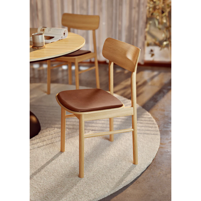 The Soma Dining Chair from Woud in Oiled Oak with Leather tucked into a dining table with coffee and a book.