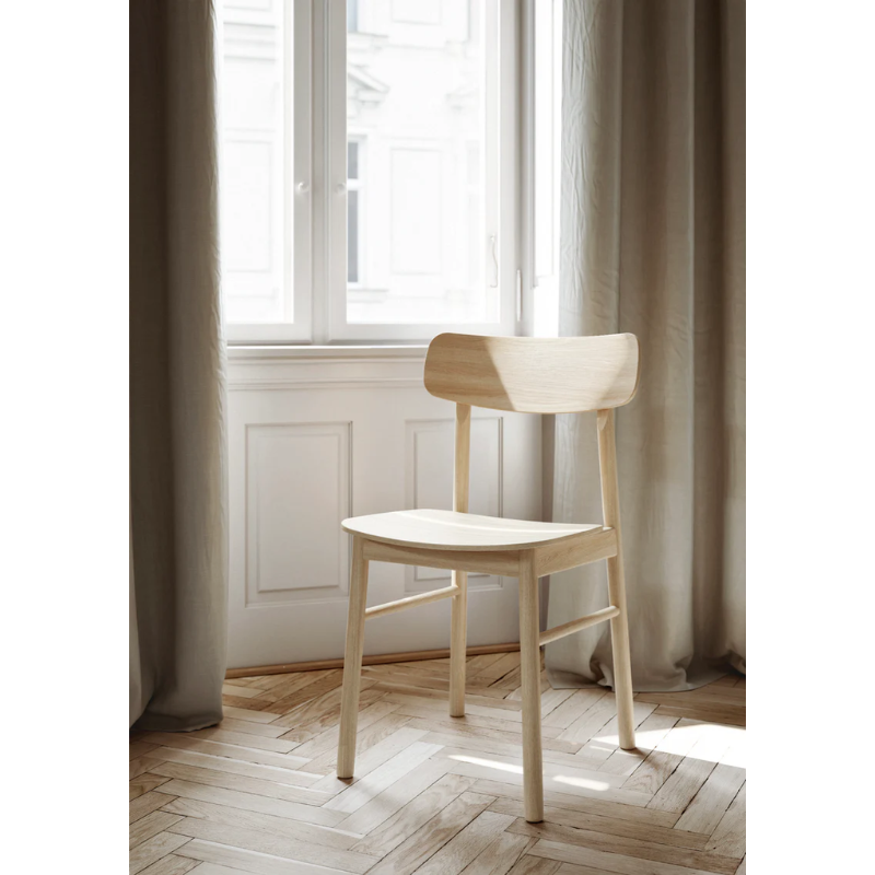 The Soma Dining Chair from Woud in White Pigmented Oak next to a window.