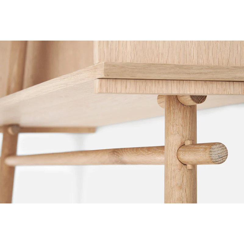 A close up showing the lower hanging bar of the Töjbox Wardrobe from Woud in white pigmented oak color.