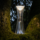 The Come Together Portable Lamp from Artemide in aluminum in a garden.