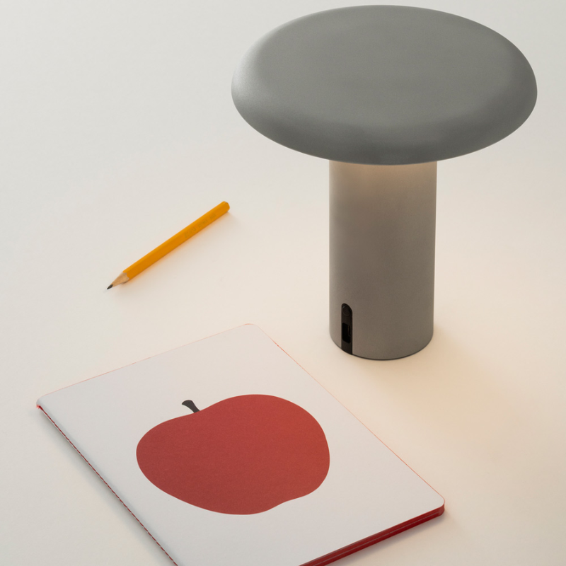 The Takku Portable Lamp from Artemide in gray in a study.